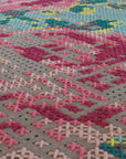 Nærbillede af tæppets sting i pink og rød på grå filtbase, som viser broderikunstens kompleksitet.