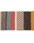 Rektangulært tæppe med striber i varme farver som brun, lilla, koral og sennep, og forskellige strik-lignende teksturer og mønstre.