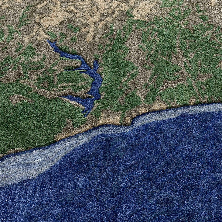 Nærbillede af PLASTIC RIVERS Niger-tæppe, der detaljeret viser flodudløb og kystlinje med dybe blå havtoner, grøn skov og beige landskab - designet som et satellitfoto gengivet i håndtuftet uld.