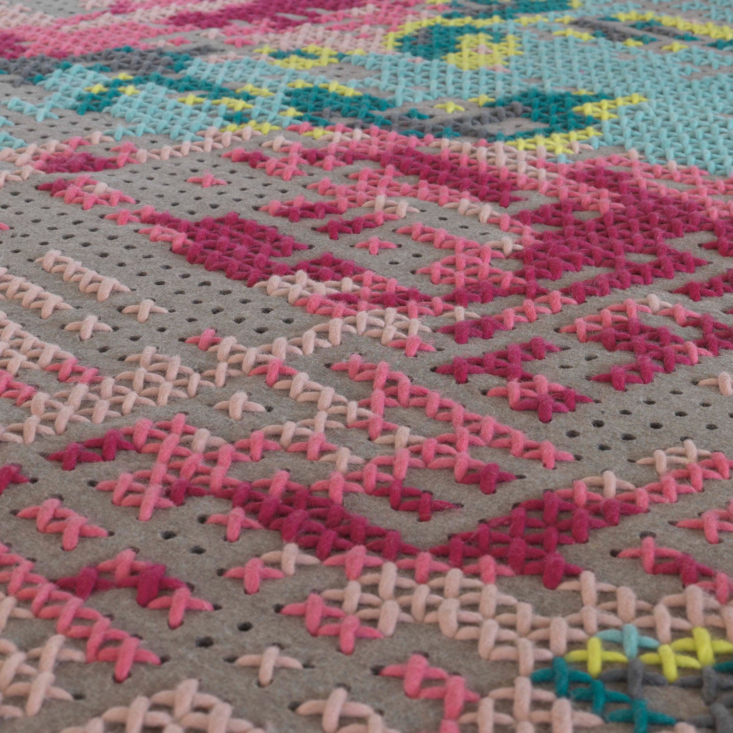 Nærbillede af tæppets sting i pink og rød på grå filtbase, som viser broderikunstens kompleksitet.